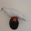 A white dove figurine with a small orange beak and a dark textured base, photographed against a plain light background.