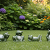 Four green frog figurines in different poses arranged on a strip of artificial grass against a plain light background.