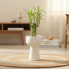 A white ceramic toilet-shaped planter or bowl with a flared base, photographed upright on a strip of green artificial grass against a plain light background.