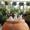 Three small white rabbit figurines with pink inner ears and black eyes, arranged on a strip of green artificial grass against a plain light background.