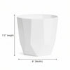 A white faceted geometric planter pot displayed on a wooden stool against a plain beige wall.