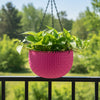 A bright pink woven basket with a scalloped rim and small black hanging loops, displayed on a wooden stool against a plain light background.