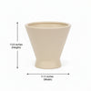 A beige ceramic planter pot with a white barcode label on the front, displayed on a dark wooden surface against a plain light gray wall.